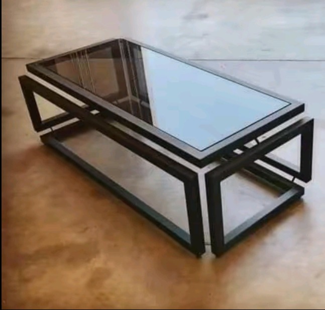 Stolik kawowy z ciemną metalową ramą i szklanym blatem, ustawiony na polerowanej podłodze.