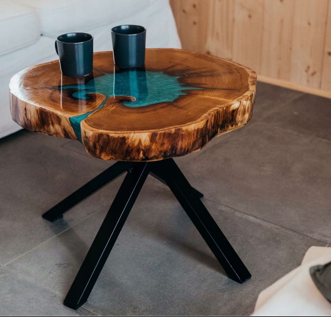 Stolik kawowy z blatem z plastra drewna z żywicą epoksydową w kolorze turkusowym, na metalowej, czarnej podstawie, z dwoma ciemnoszarymi kubkami na blacie.