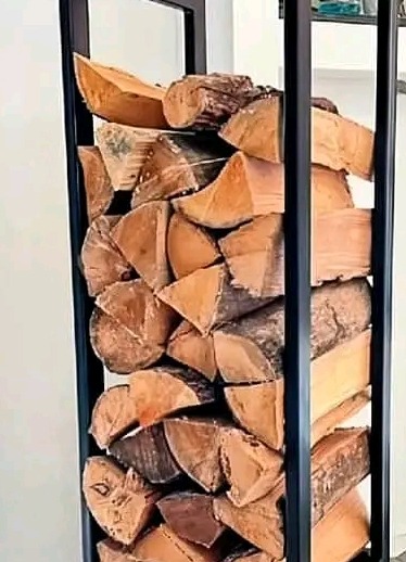 Metalowy stojak na drewno kominkowe, wypełniony pociętymi kawałkami drewna o różnej wielkości i fakturze.