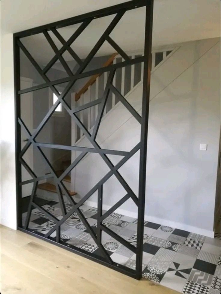 Nowoczesna, ażurowa ścianka działowa z czarnych profili na tle schodów i patchworkowej podłogi z płytek.
