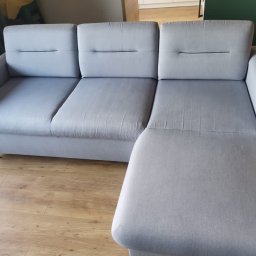 Perfect Clean Bartosz Reus - Szara, modułowa kanapa z podnóżkiem, ustawiona na drewnianej podłodze, widoczna z boku, z trzema siedziskami i subtelnymi przeszyciami.