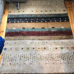 Perfect Clean Bartosz Reus - Wielobarwny dywan w etniczne wzory, częściowo odkurzany, widoczne drewniane deski podłogowe i fragment sofy.