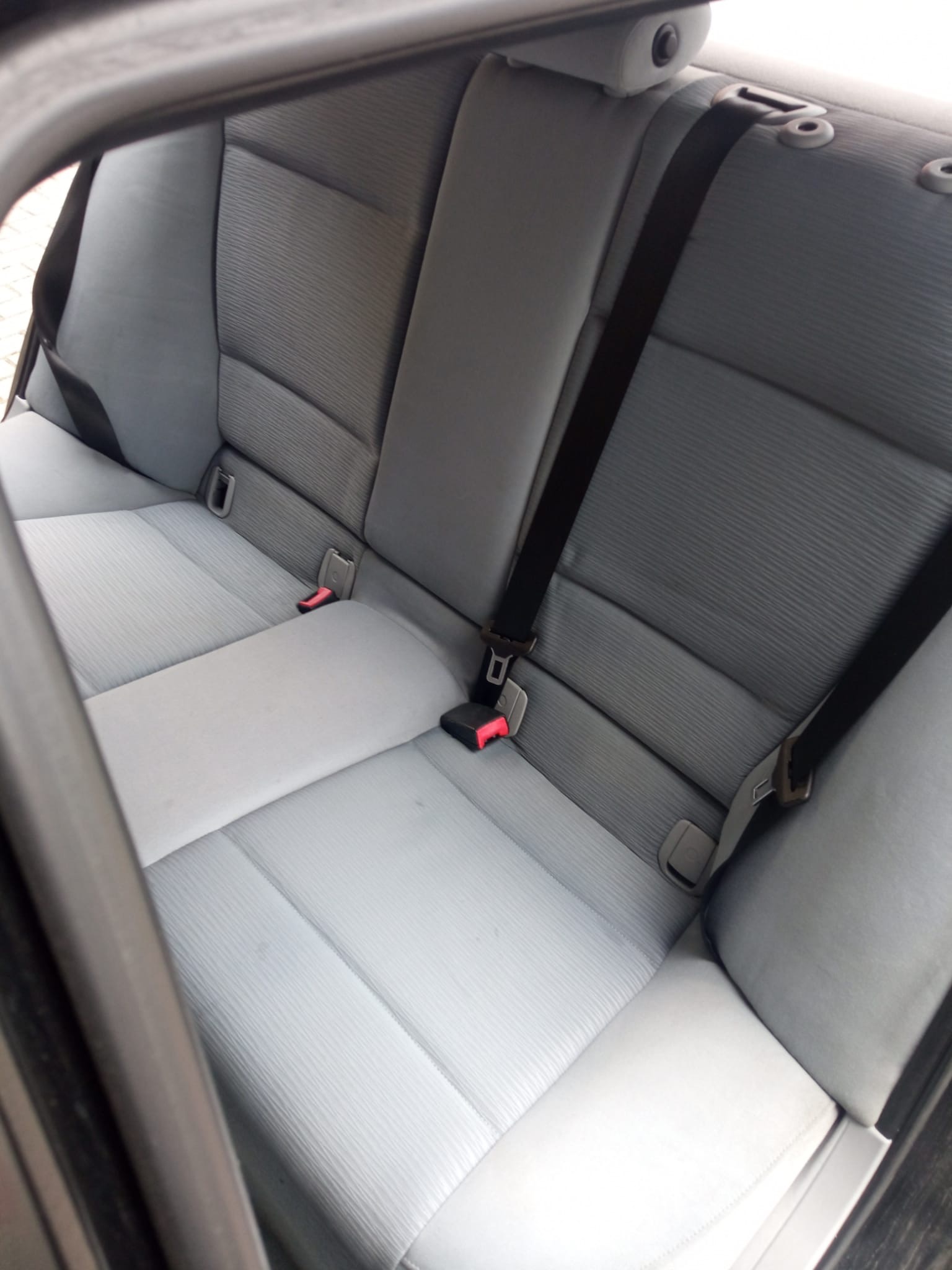 Szare, tekstylne siedzenia tylne samochodu z pasami bezpieczeństwa, widok z wnętrza pojazdu.