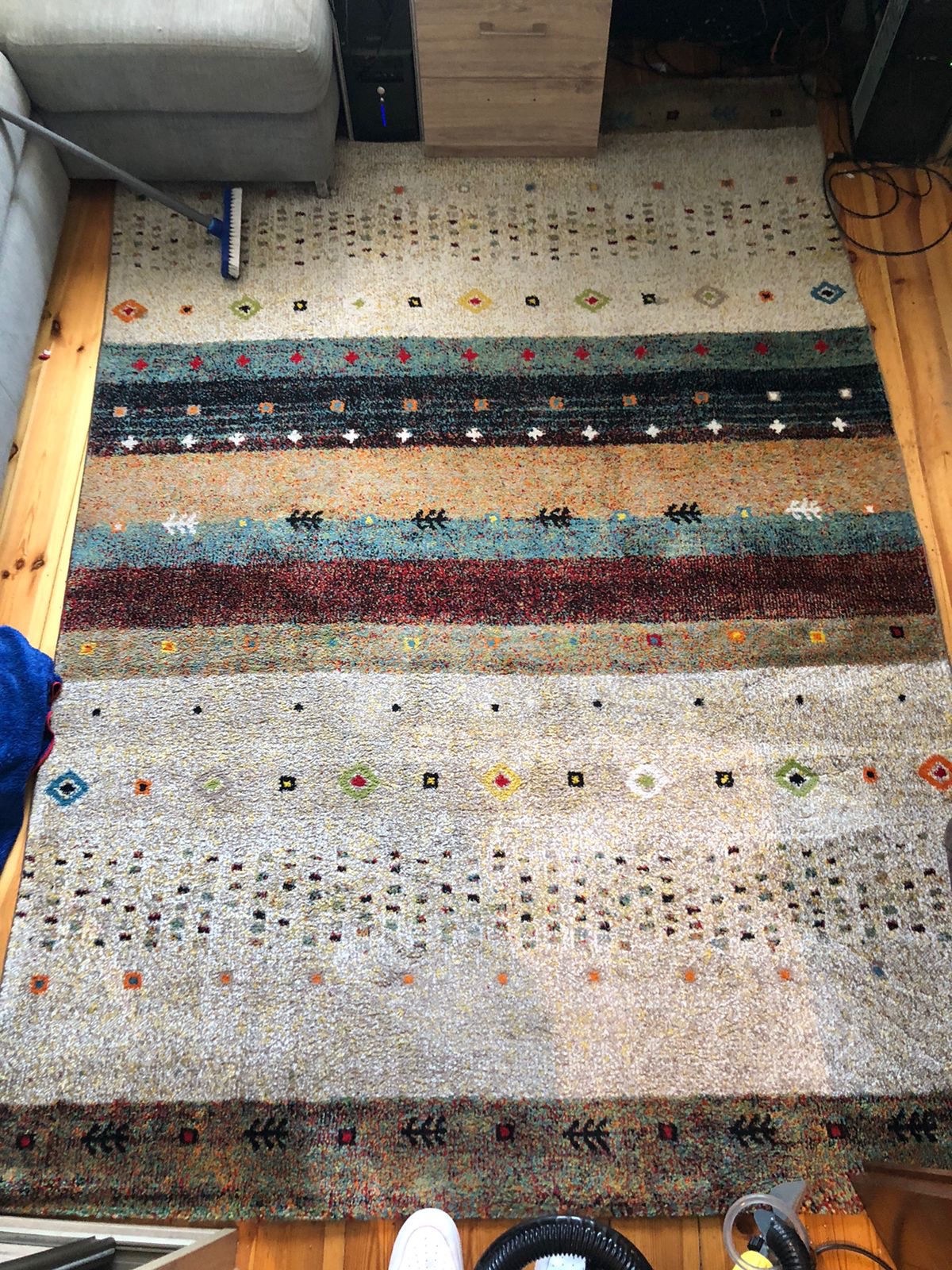 Wielobarwny dywan w etniczne wzory, częściowo odkurzany, widoczne drewniane deski podłogowe i fragment sofy.