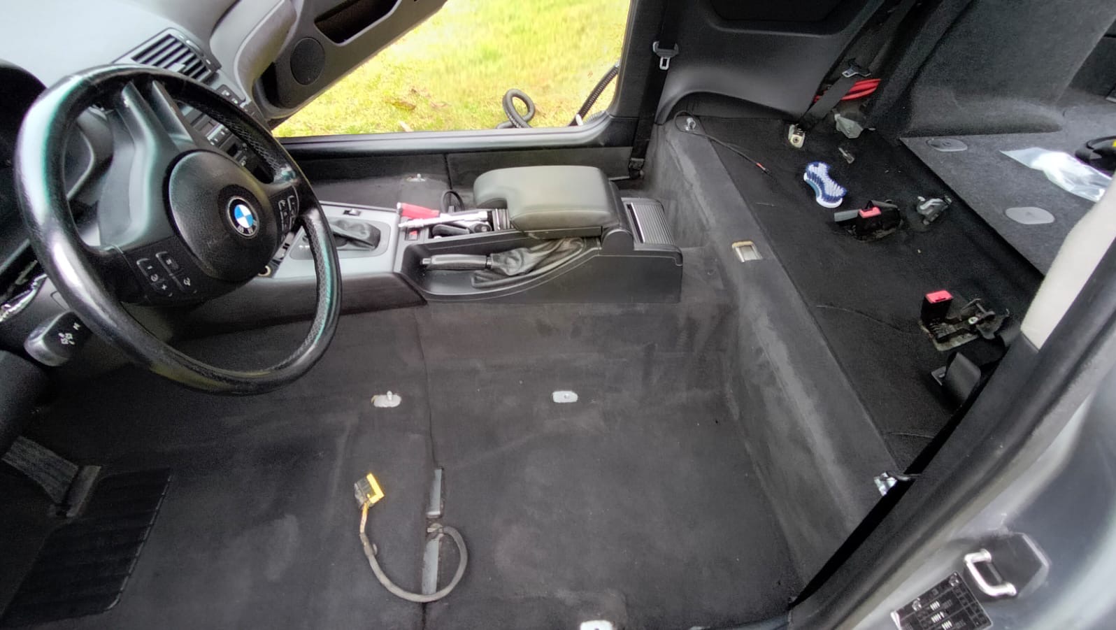 Wnętrze samochodu marki BMW, zdemontowane fotele i elementy tapicerki, przygotowane do czyszczenia. Widoczne ślady po wodzie na dywanikach podłogowych.