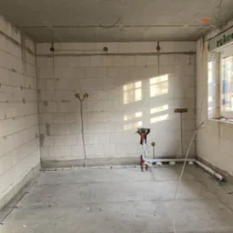 Surowy stan wnętrza z widocznymi przewodami elektrycznymi w ścianach i podłodze, przygotowanego do dalszych prac wykończeniowych. Widoczne puszki instalacyjne.