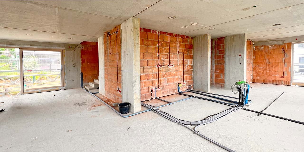 Wnętrze w trakcie instalacji elektrycznej: widoczne kable i rury prowadzone po podłodze i ścianach z cegły, przygotowane do dalszych prac wykończeniowych.