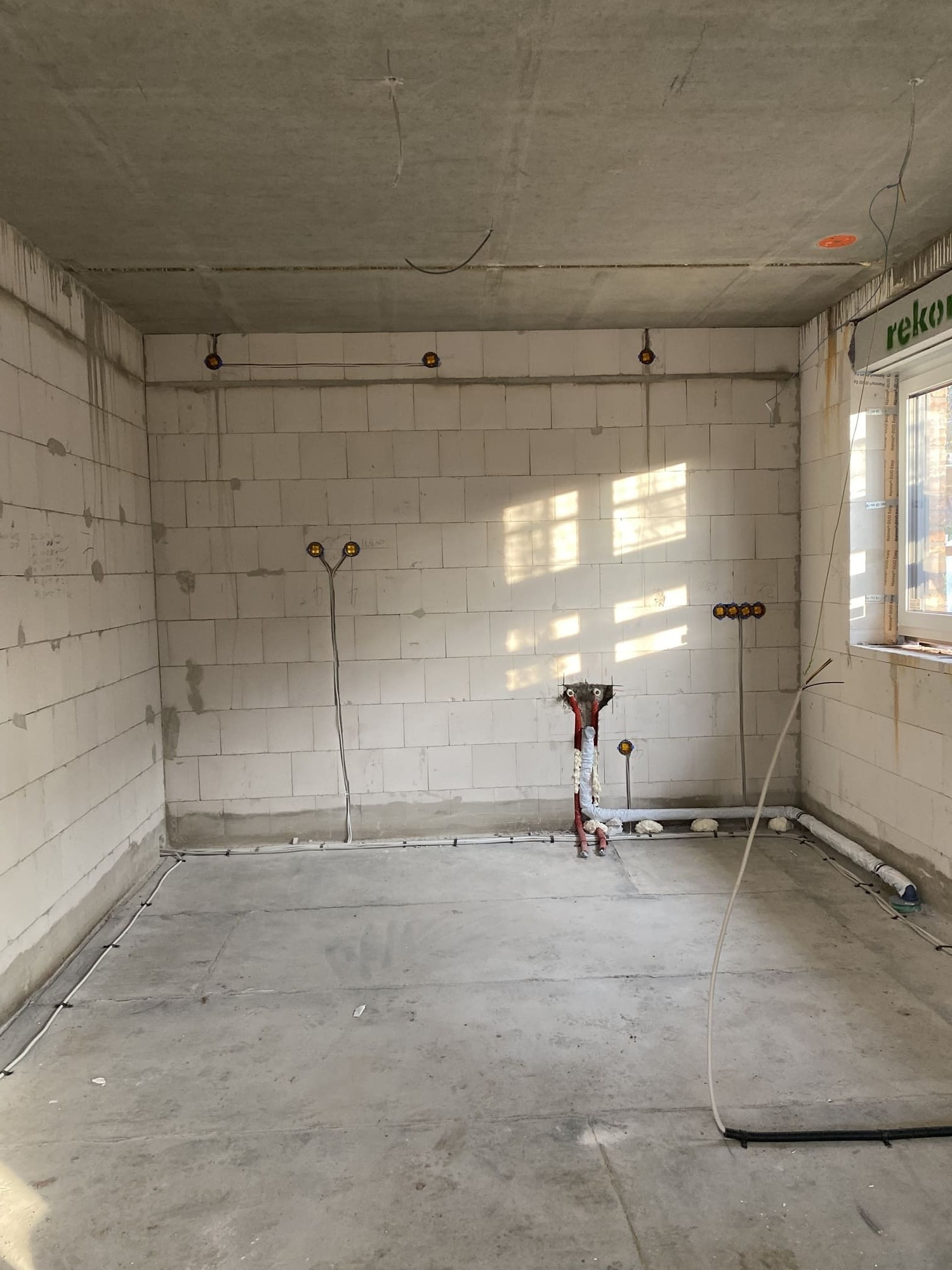 Surowy stan wnętrza z widocznymi przewodami elektrycznymi w ścianach i podłodze, przygotowanego do dalszych prac wykończeniowych. Widoczne puszki instalacyjne.