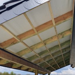 for your comfort - Konin: Widok od dołu na konstrukcję drewnianą dachu z izolacją i częściowo zamontowaną podbitką dachową z paneli PCV.