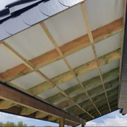 Konin: Widok od dołu na konstrukcję drewnianą dachu z izolacją i częściowo zamontowaną podbitką dachową z paneli PCV.