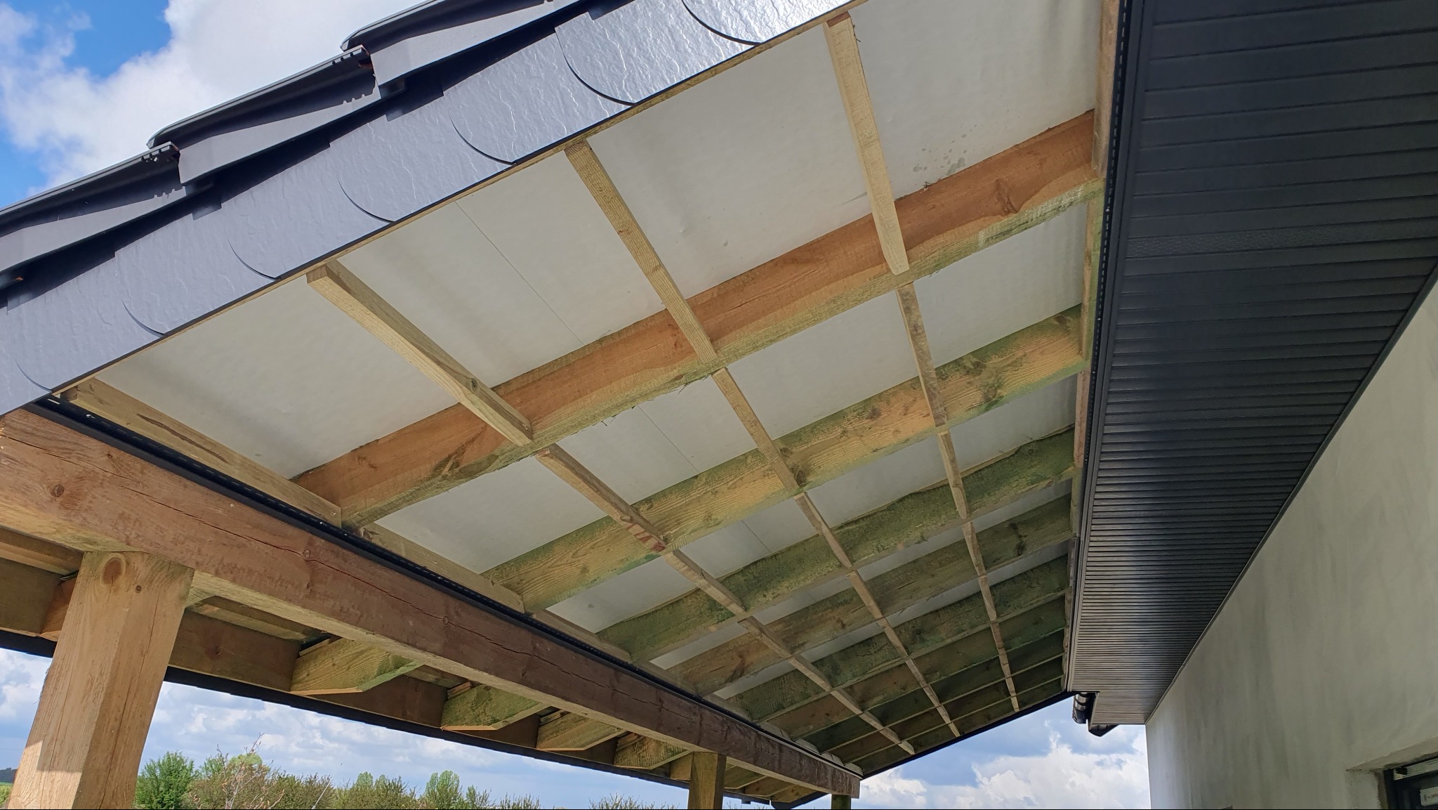 Konin: Widok od dołu na konstrukcję drewnianą dachu z izolacją i częściowo zamontowaną podbitką dachową z paneli PCV.