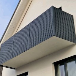 IronTech - Nowoczesny balkon z szarą, poziomą okładziną lamelową, zamontowany przy białej ścianie budynku z widocznymi oknami.