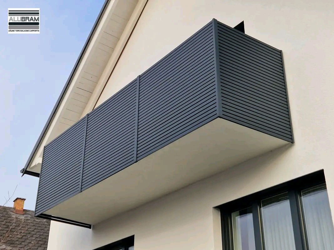 Nowoczesny balkon z szarą, poziomą okładziną lamelową, zamontowany przy białej ścianie budynku z widocznymi oknami.