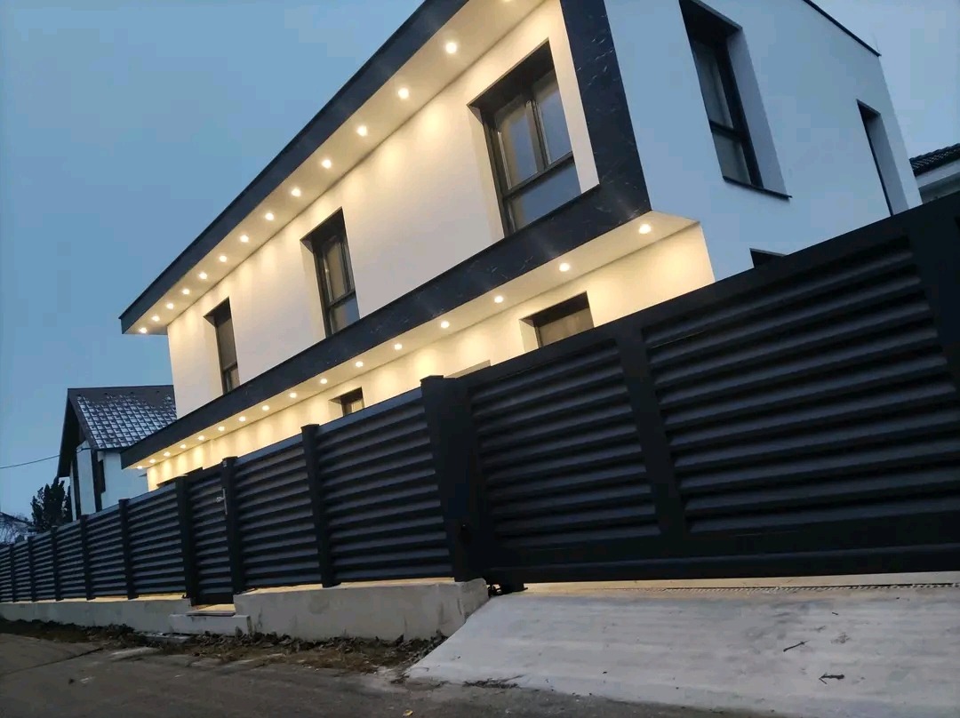 Nowoczesne ogrodzenie panelowe w kolorze antracytowym, z poziomymi lamelami, dopasowane do elewacji domu z oświetleniem punktowym.