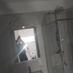 Grzegorz Pałasz - Wykończona łazienka z kabiną prysznicową typu walk-in, wykończona płytkami imitującymi marmur z żyłami w kolorze miedzi, widoczne odbicie osoby robiącej zdjęcie w lustrze.