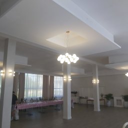 Grzegorz Pałasz - Jasne, przestronne wnętrze sali bankietowej w Trzebielinie po remoncie, z dekoracyjnym oświetleniem sufitowym, kolumnami i przygotowanymi stołami.