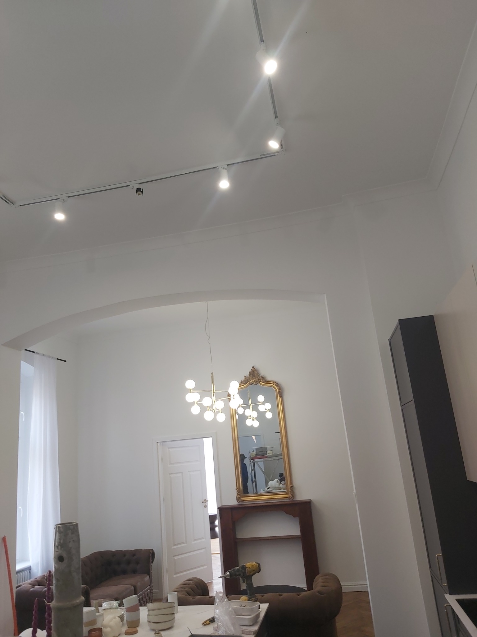 Wnętrze mieszkania po odświeżeniu ścian, widoczne ślady po pracach wykończeniowych, w tle stylowe meble i oświetlenie szynowe na suficie.