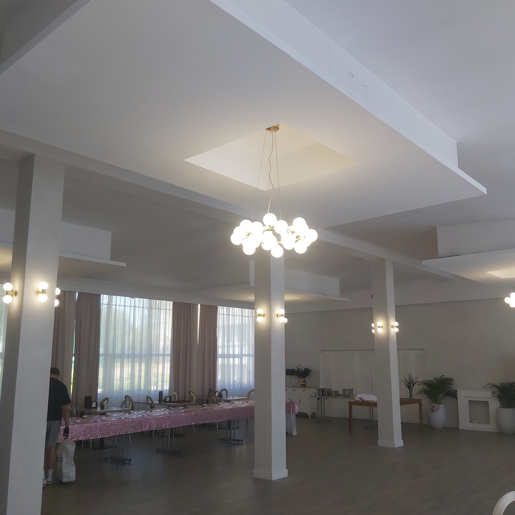 Jasne, przestronne wnętrze sali bankietowej w Trzebielinie po remoncie, z dekoracyjnym oświetleniem sufitowym, kolumnami i przygotowanymi stołami.