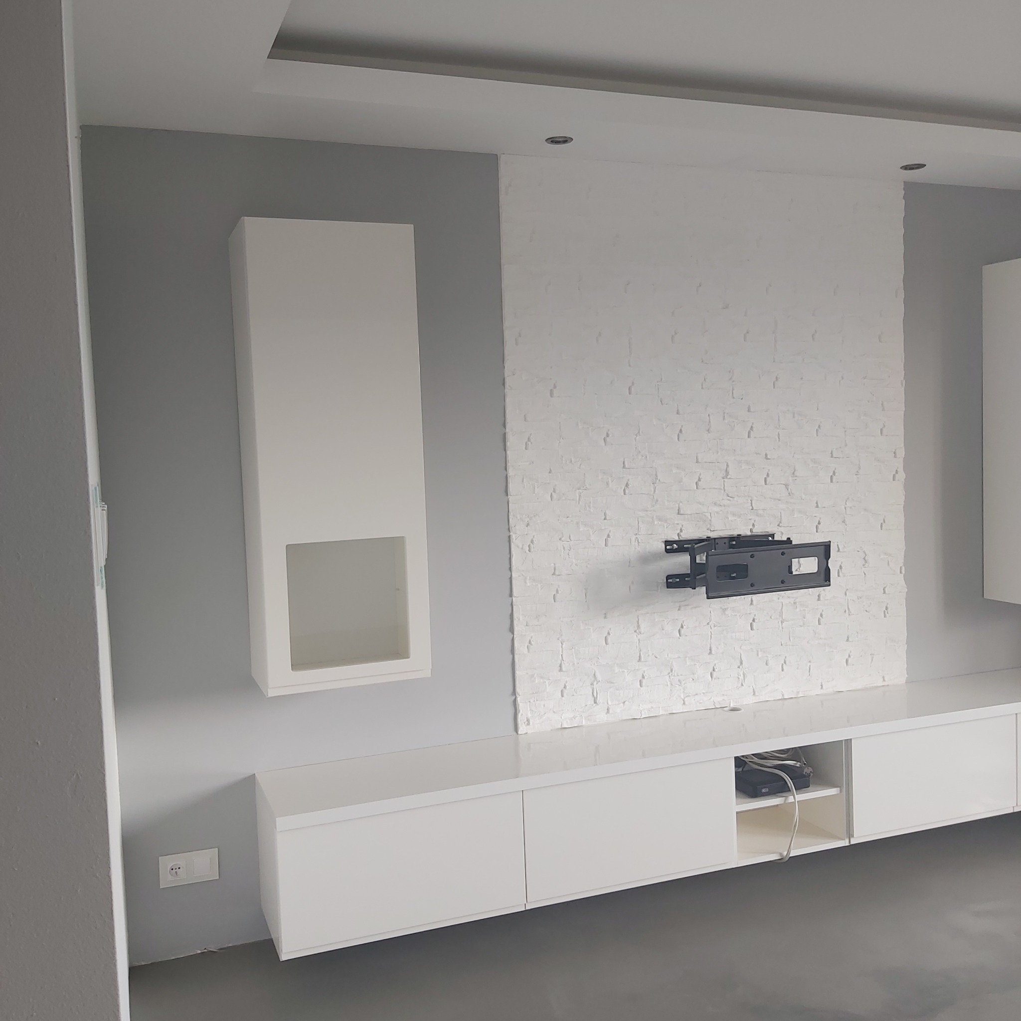 Nowoczesny salon z białymi meblami na wymiar, ściana z dekoracyjnej białej cegły i uchwytem do telewizora.