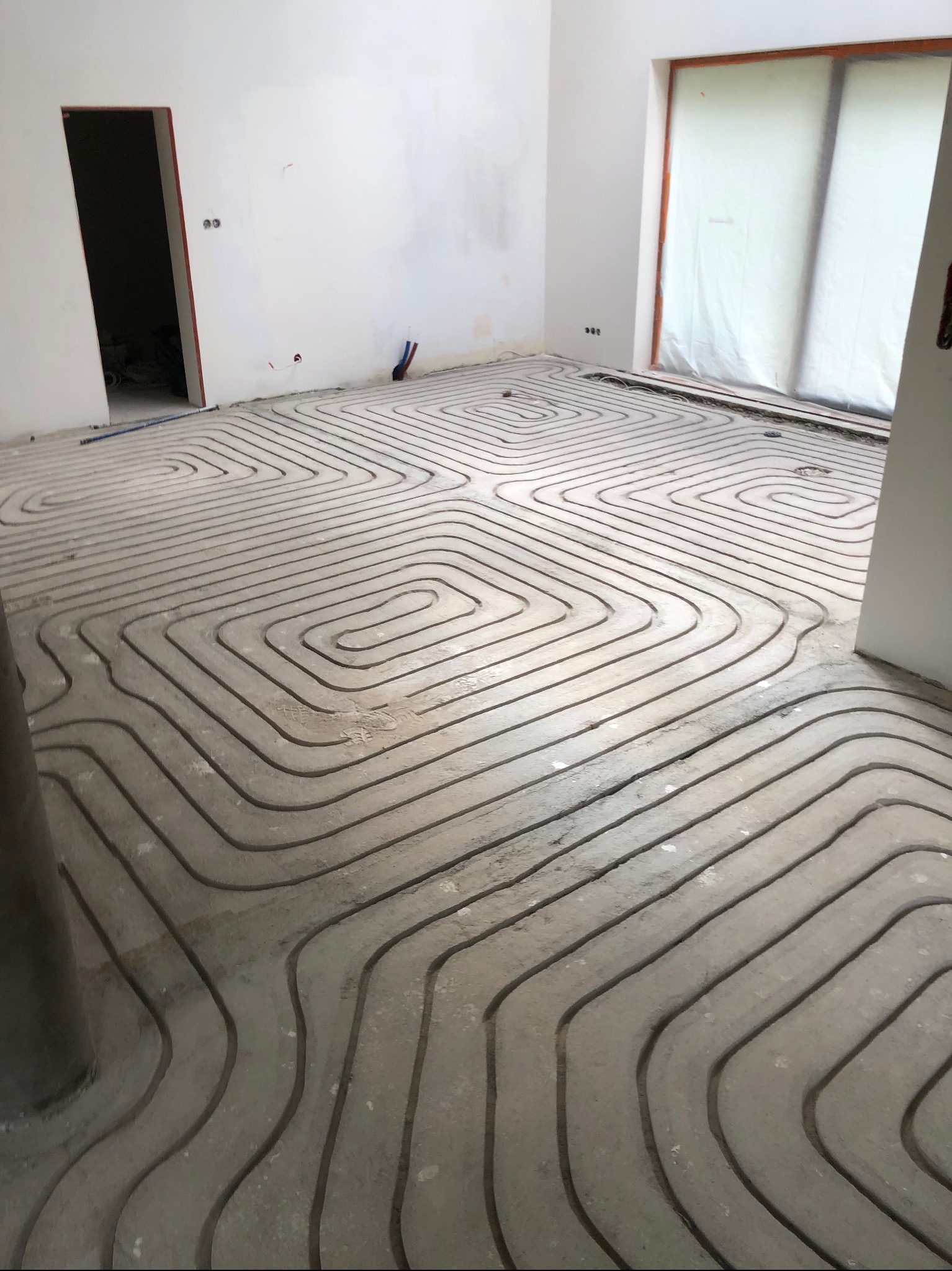 Instalacja ogrzewania podłogowego wylewka betonowa z widocznymi rurami w nowym domu, przygotowana do dalszych prac wykończeniowych.