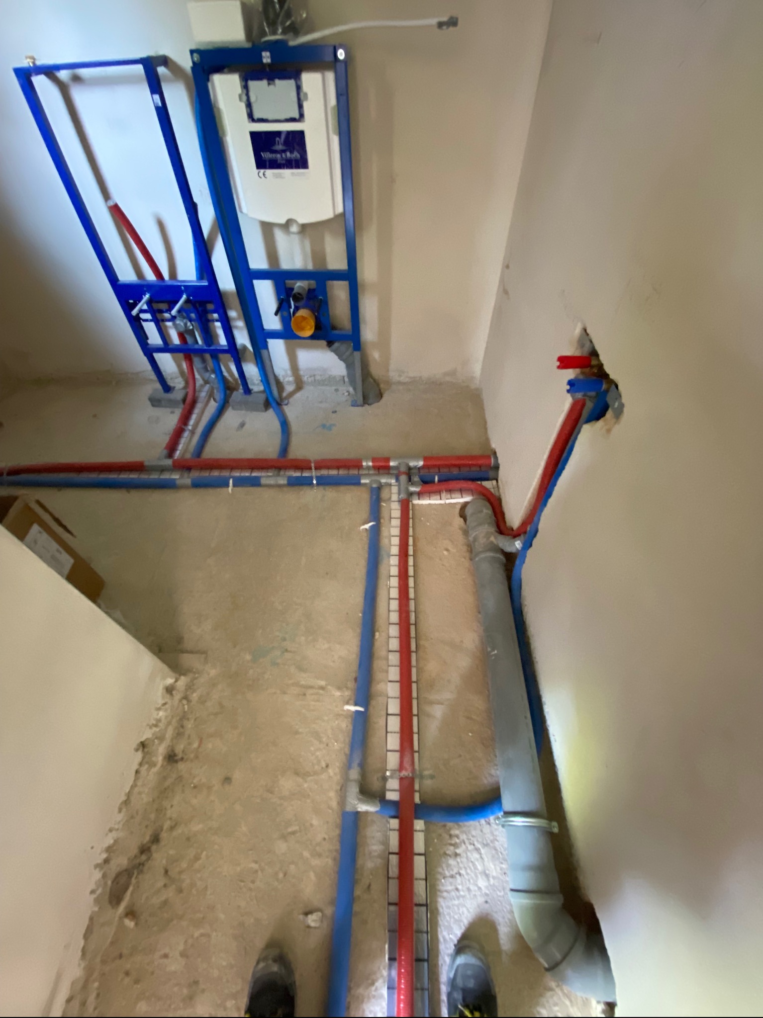 Wnętrze łazienki w trakcie montażu instalacji wodno-kanalizacyjnej podtynkowo, widoczne rury PEX w kolorze czerwonym i niebieskim, stelaż podtynkowy WC Villeroy & Boch z elementami mocującymi,...