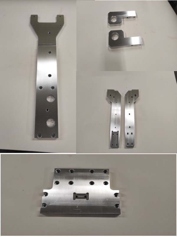 Aluminiowe elementy obrobione z dużą precyzją, widoczne otwory i frezowania, różne kształty i rozmiary, ułożone na białym tle.