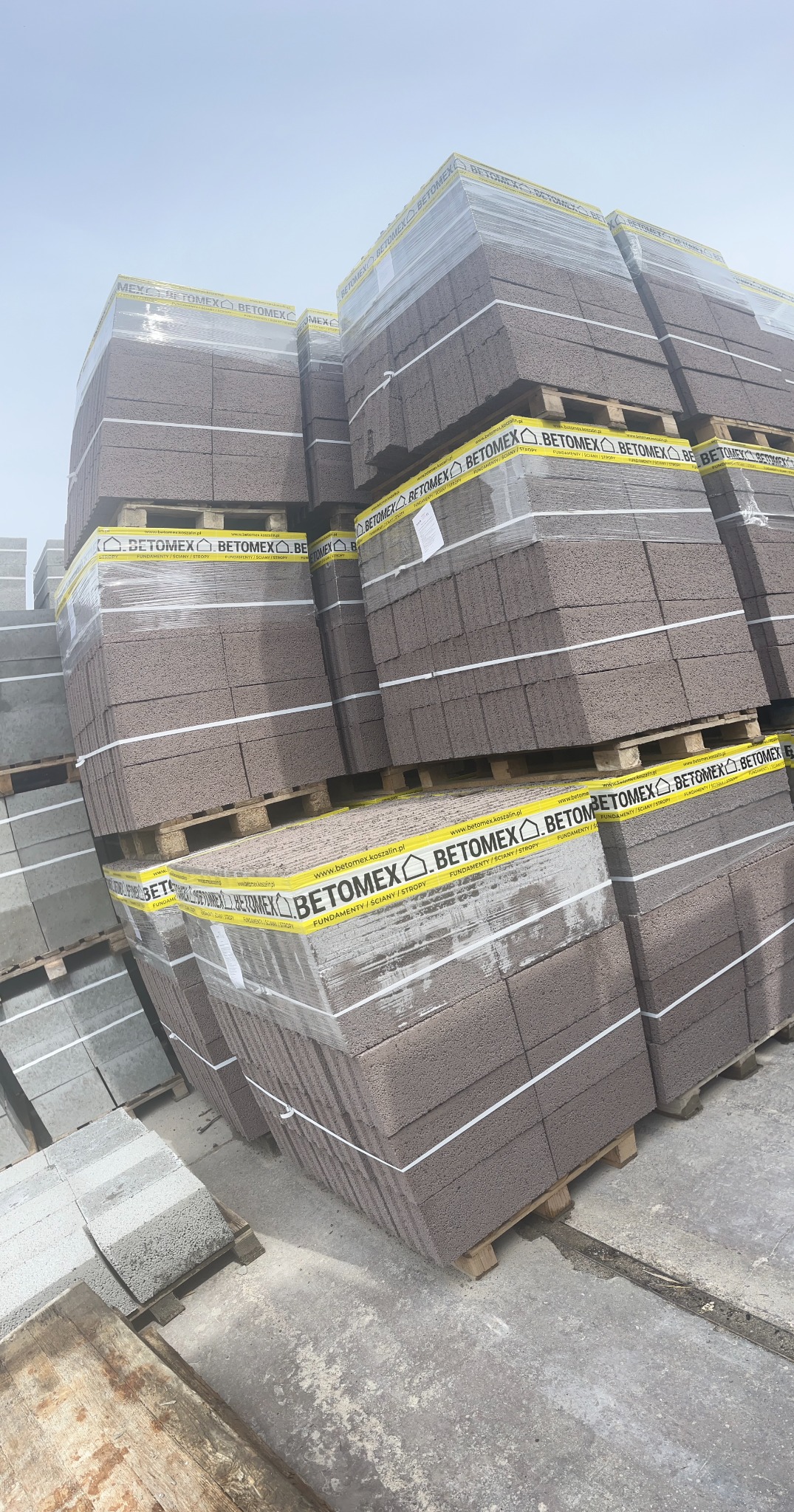 Palety z bloczkami z keramzytu Betomex, zabezpieczone folią i taśmą z logo producenta, składowane na placu budowy.