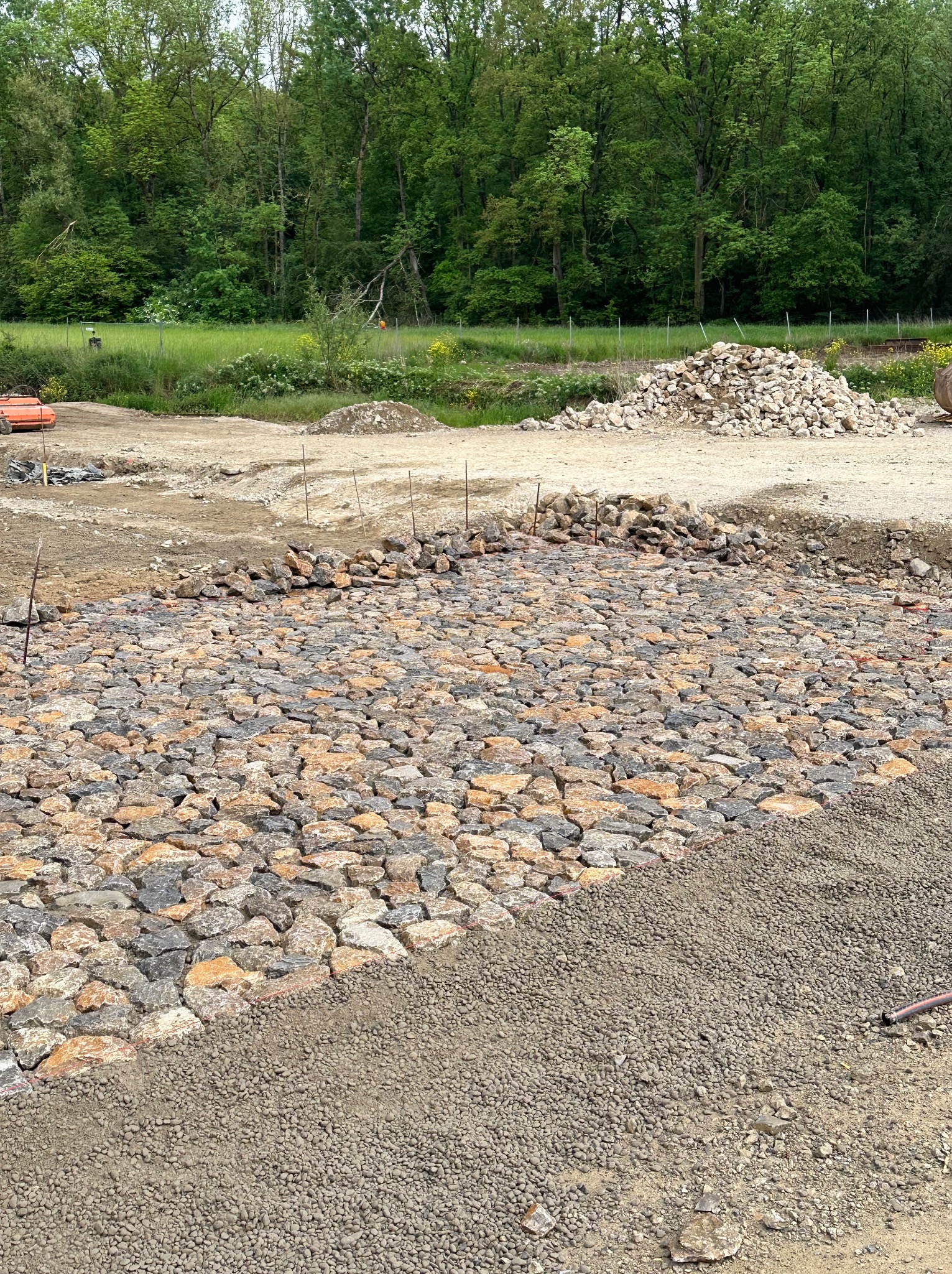 Wykonywanie podbudowy z kamienia łamanego na utwardzanej drodze, widoczny nasyp z drobnego kruszywa i stos kamieni w tle.