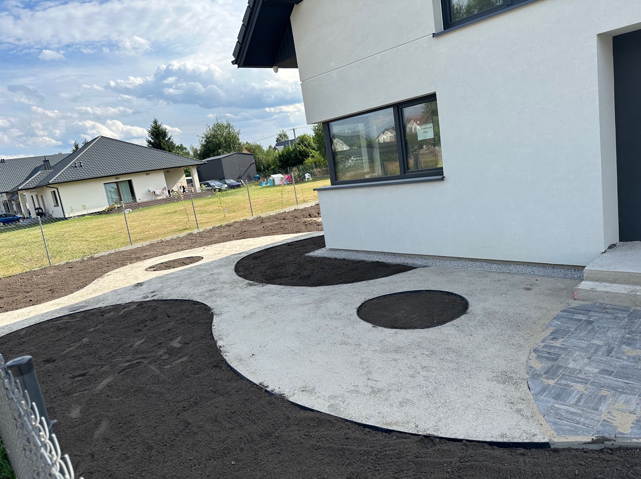 Przygotowany teren pod aranżację ogrodu z wysypanym kruszywem i wyznaczonymi rabatami z czarnej ziemi, widok z boku domu.