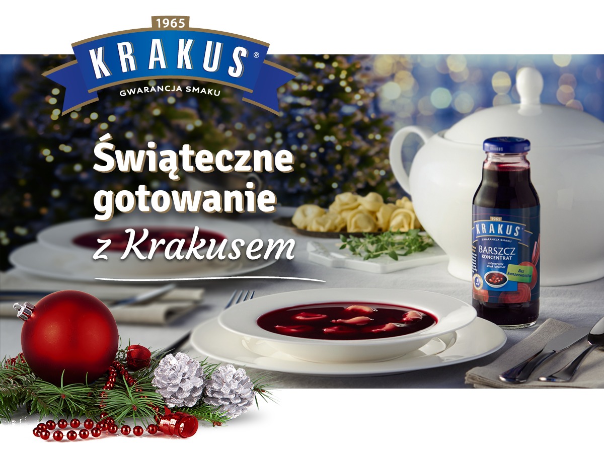 Świąteczny stół z talerzem czerwonego barszczu, pierogami w tle, butelką koncentratu Krakus i dekoracjami bożonarodzeniowymi, w tym czerwoną bombką i srebrnymi szyszkami.