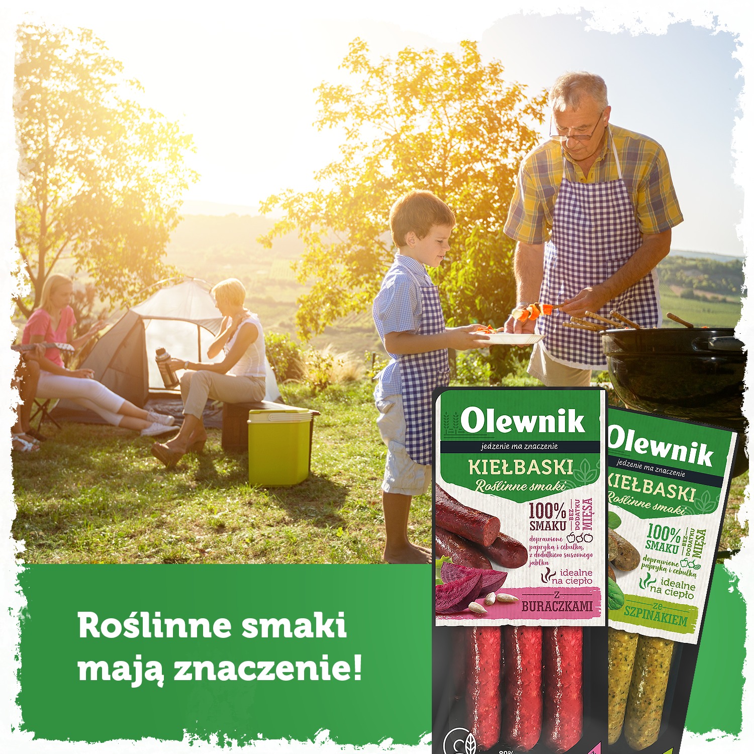 Rodzinny piknik na trawie: dziadek i wnuk przygotowują szaszłyki przy grillu, w tle mama z córką siedzą przy namiocie, obok leżą opakowania kiełbasek roślinnych.