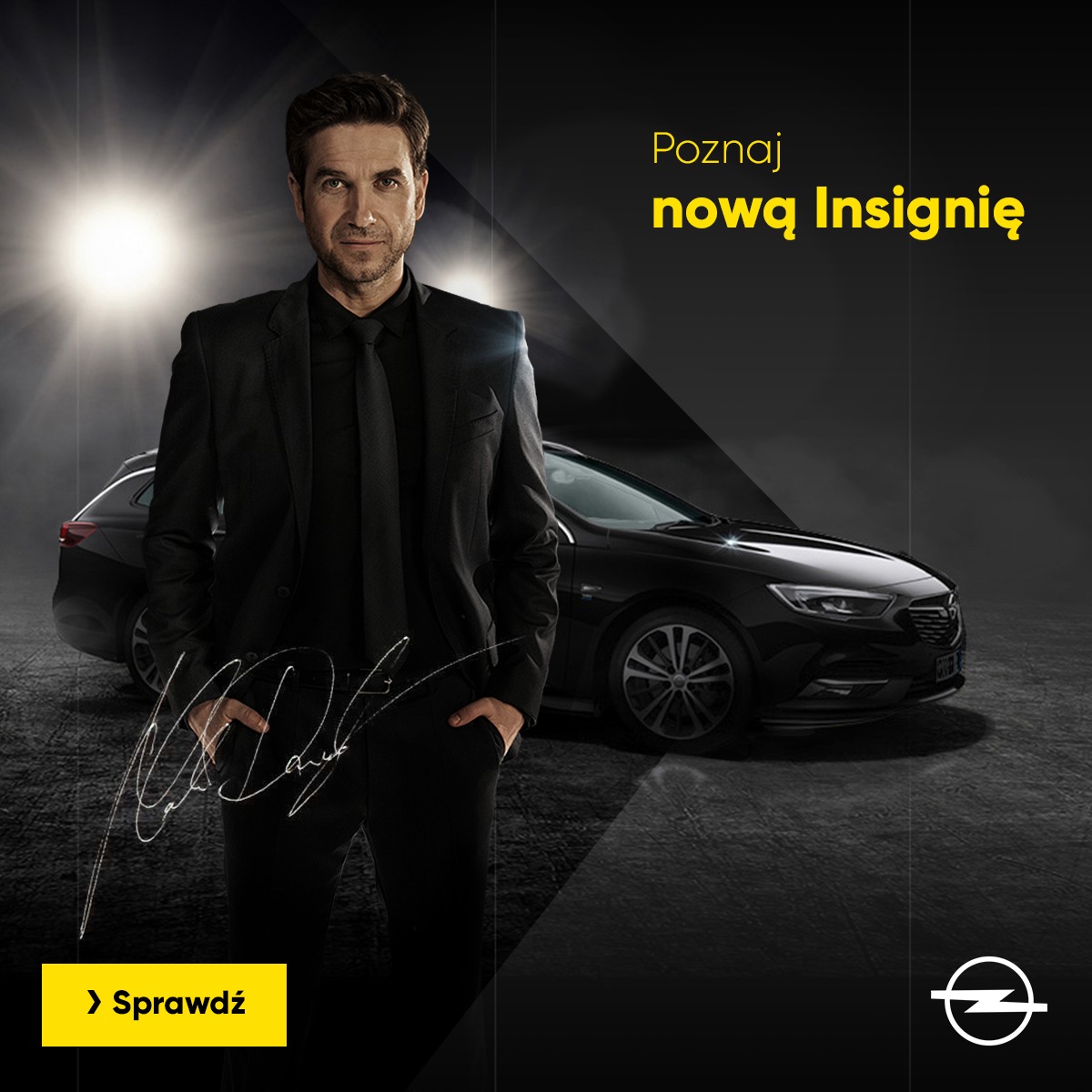 Mężczyzna w garniturze stoi obok czarnej Insigni na ciemnym tle z promieniami światła, podpis na pierwszym planie, reklama nowej Insigni.