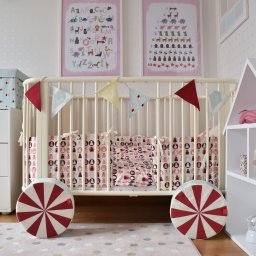 PODLASKA AGENCJA BUDOWLANA MARTA I ADAM BUCZYŃSCY SPÓŁKA CYWILNA - Pokój dziecięcy z białym łóżeczkiem, girlandą z trójkątów, poduszkami w misie, komodą z pudełkiem, regałem w kształcie domku i plakatami edukacyjnymi na ścianie w gwiazdki.