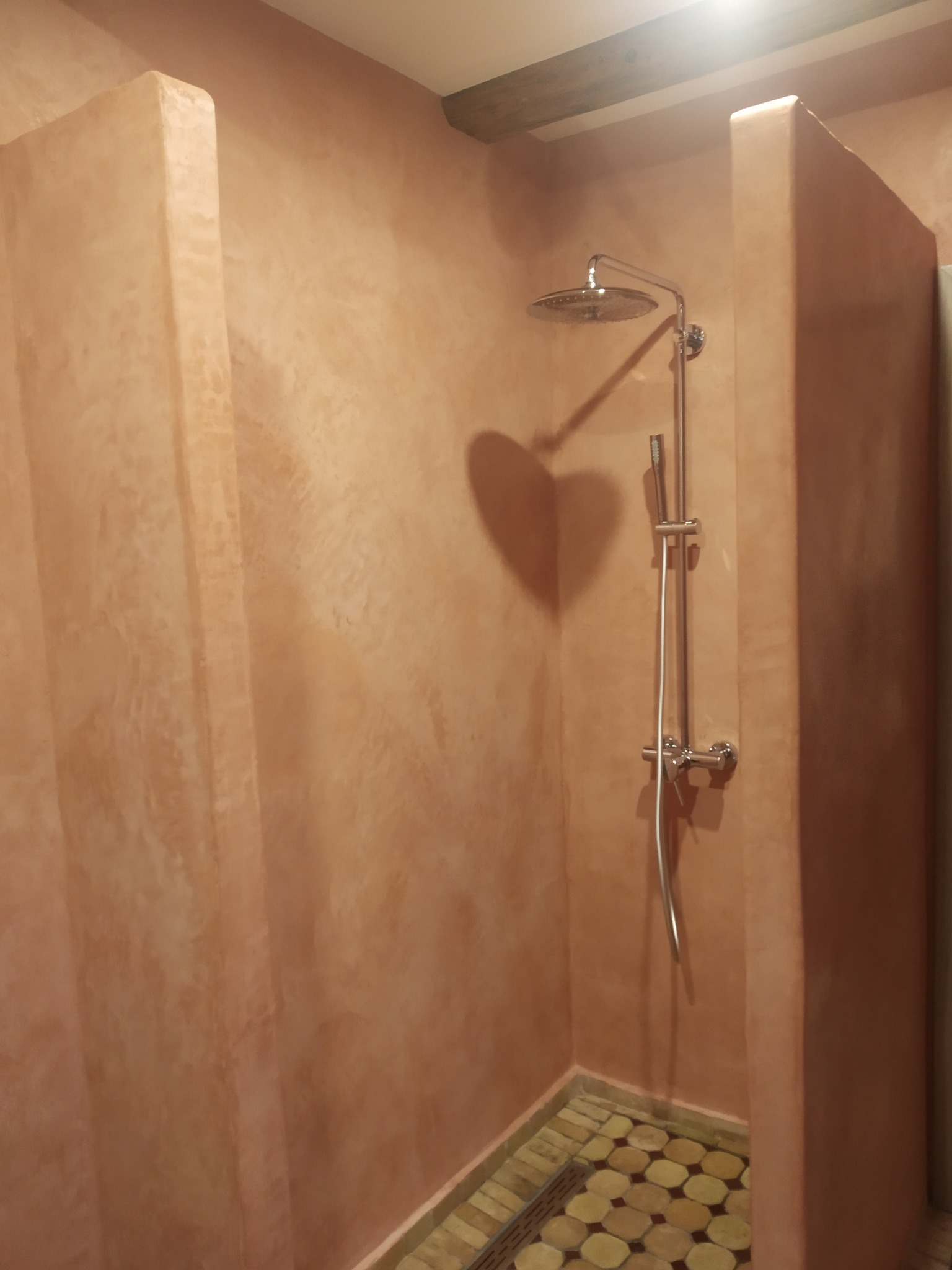 Wykończona kabina prysznicowa z beżowymi ścianami o fakturze trawertynu i mozaikową podłogą z okrągłych płytek.