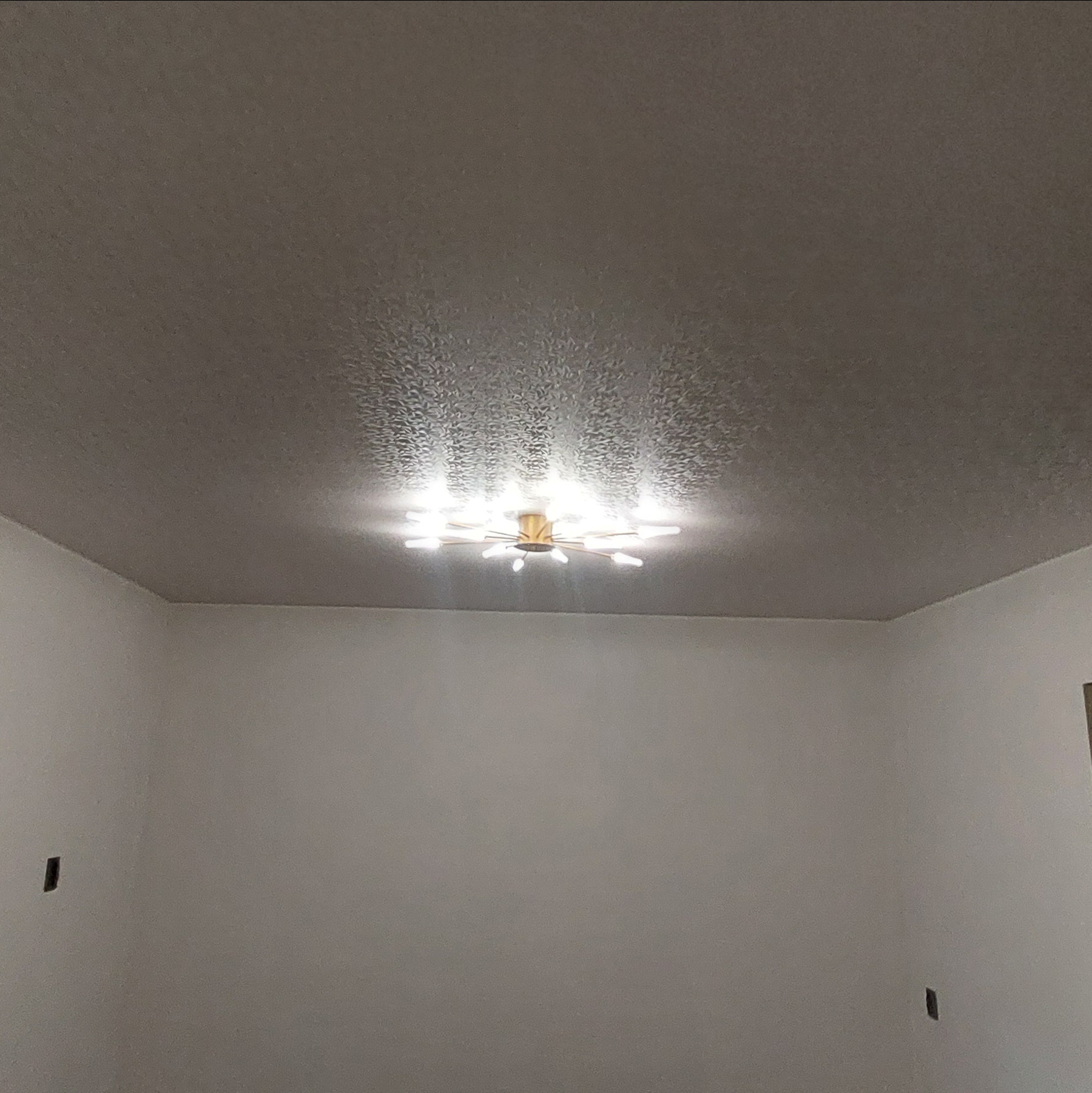 Jasny pokój z gładkim, szarym sufitem z delikatną fakturą i nowoczesną lampą sufitową w kształcie gwiazdy. Minimalistyczne wnętrze.