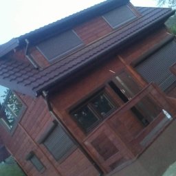 Filip Grabiński Nowoczesne Budownictwo - Drewniany dom szkieletowy z brązowym dachem i roletami zewnętrznymi, widok z boku pod kątem.