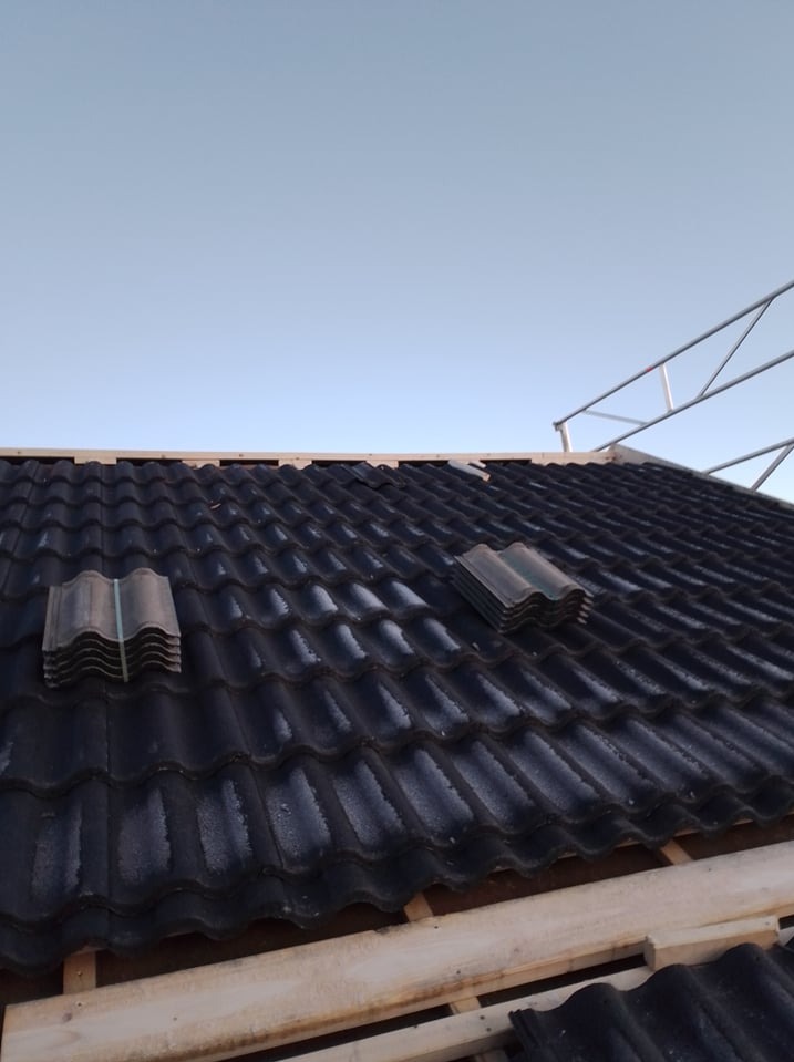 Montaż czarnej blachodachówki na nowym dachu, widoczne pakiety płytek i drewniane łaty pod konstrukcją.