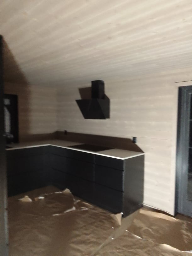 Wnętrze w trakcie wykańczania: czarna zabudowa kuchenna z białym blatem i czarnym okapem na tle boazerii, podłoga zabezpieczona folią malarską.