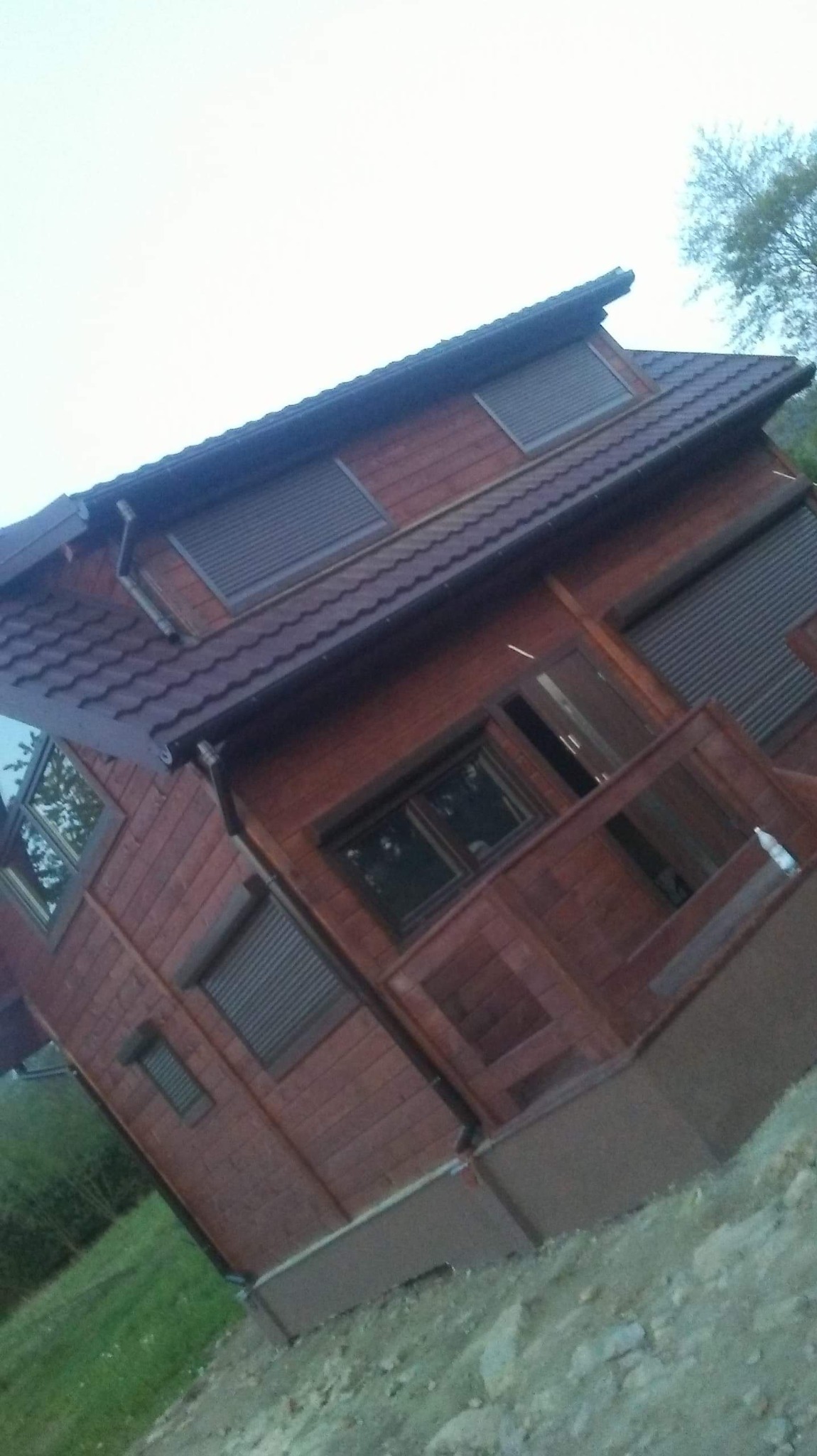 Drewniany dom szkieletowy z brązowym dachem i roletami zewnętrznymi, widok z boku pod kątem.