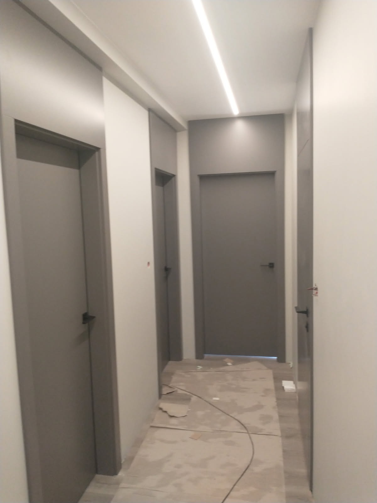 Korytarz w odcieniach szarości z trzema zamontowanymi drzwiami o minimalistycznym designie. Podłoga zabezpieczona kartonem falistym.