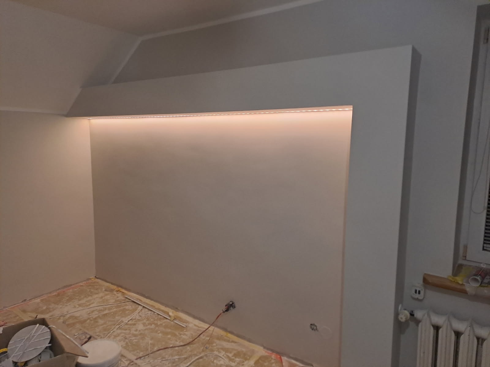 Ściana po malowaniu z wnęką oświetloną LED, widoczne przygotowania do układania podłogi. Gładkie, jasne ściany i ciepłe światło tworzą nowoczesny wygląd wnętrza.