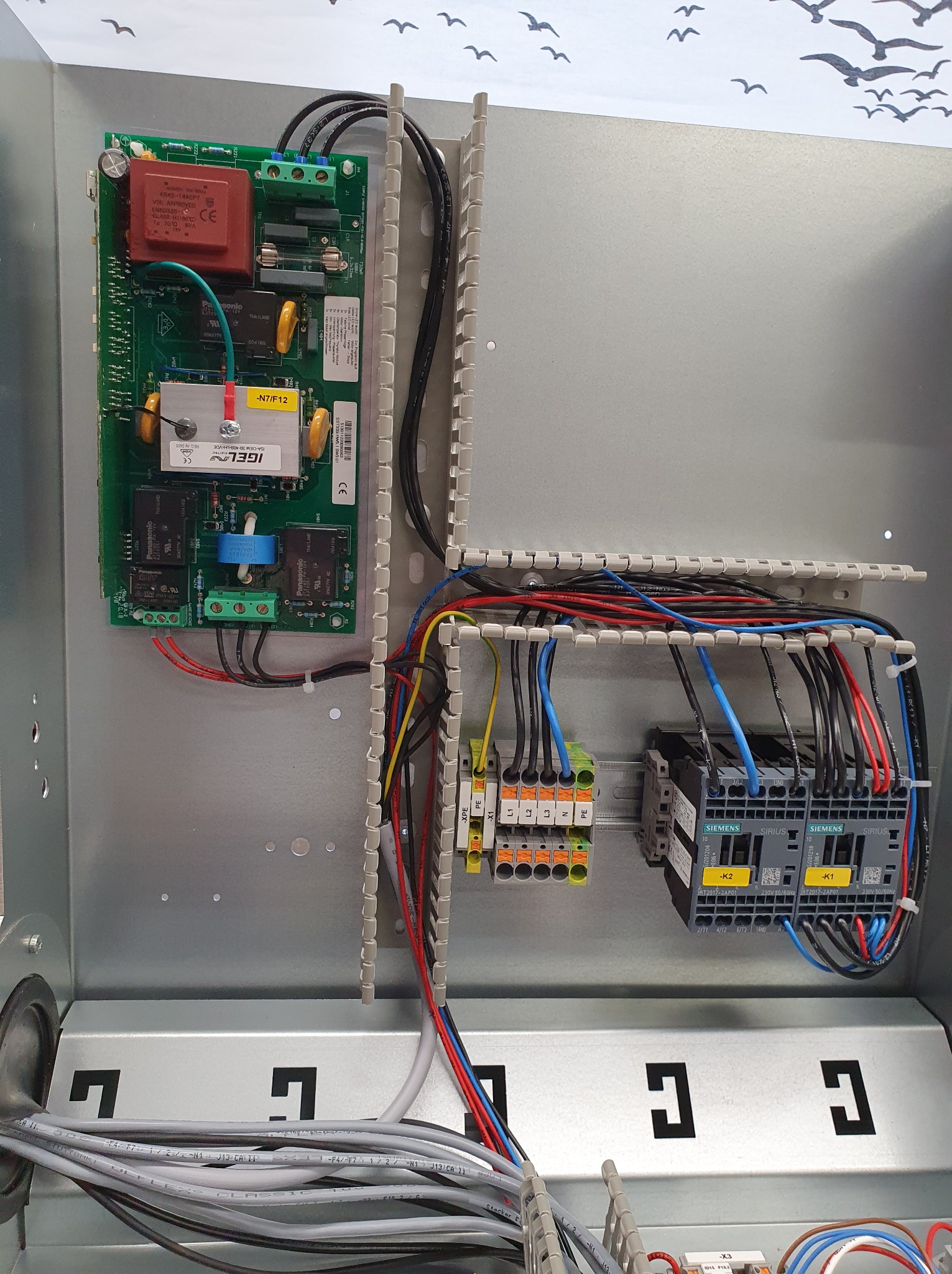 Wnętrze szafy sterowniczej z zamontowaną płytą główną, blokami zaciskowymi i przekaźnikami Siemens Sirius, widoczne różnokolorowe przewody i elementy montażowe.