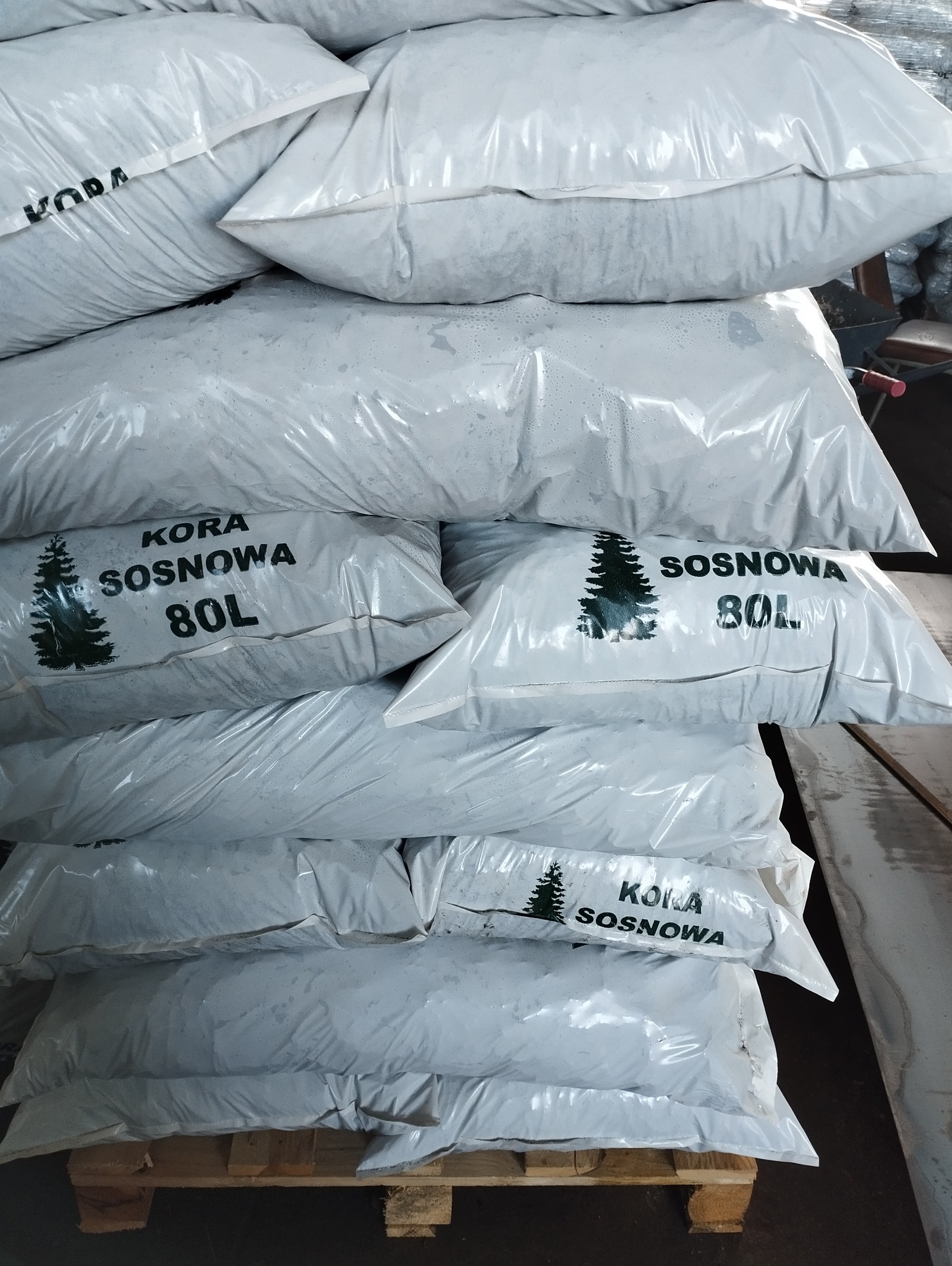 Stos worków z korą sosnową 80L, ułożonych na palecie, widoczne napisy i grafika drzewka na workach.