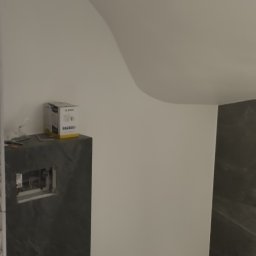 Yurii Drohomyretskyi KUB - Nowoczesna toaleta podwieszana w łazience z szarą marmurową okładziną i białą ścianą pod skosem. Widoczna instalacja podtynkowa i pudełko na blacie.