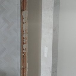 Yurii Drohomyretskyi KUB - Wykończenie otworu drzwiowego płytkami imitującymi kamień, widoczna ściana z wzorem jodełki i zabezpieczona podłoga w trakcie prac.