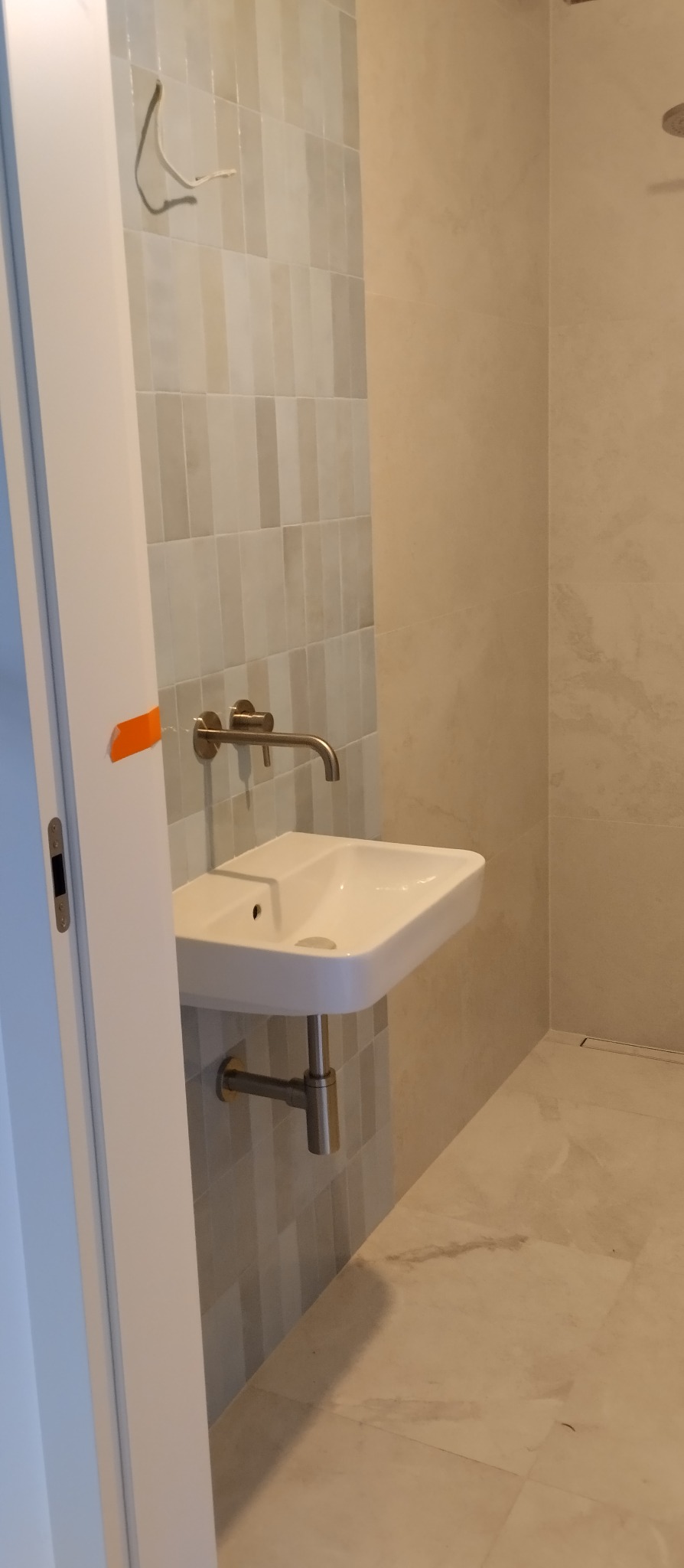 Nowoczesna łazienka po remoncie: biała umywalka nablatowa z chromowaną baterią na tle ściany z płytek w odcieniach szarości i beżu, widoczny fragment kabiny prysznicowej.