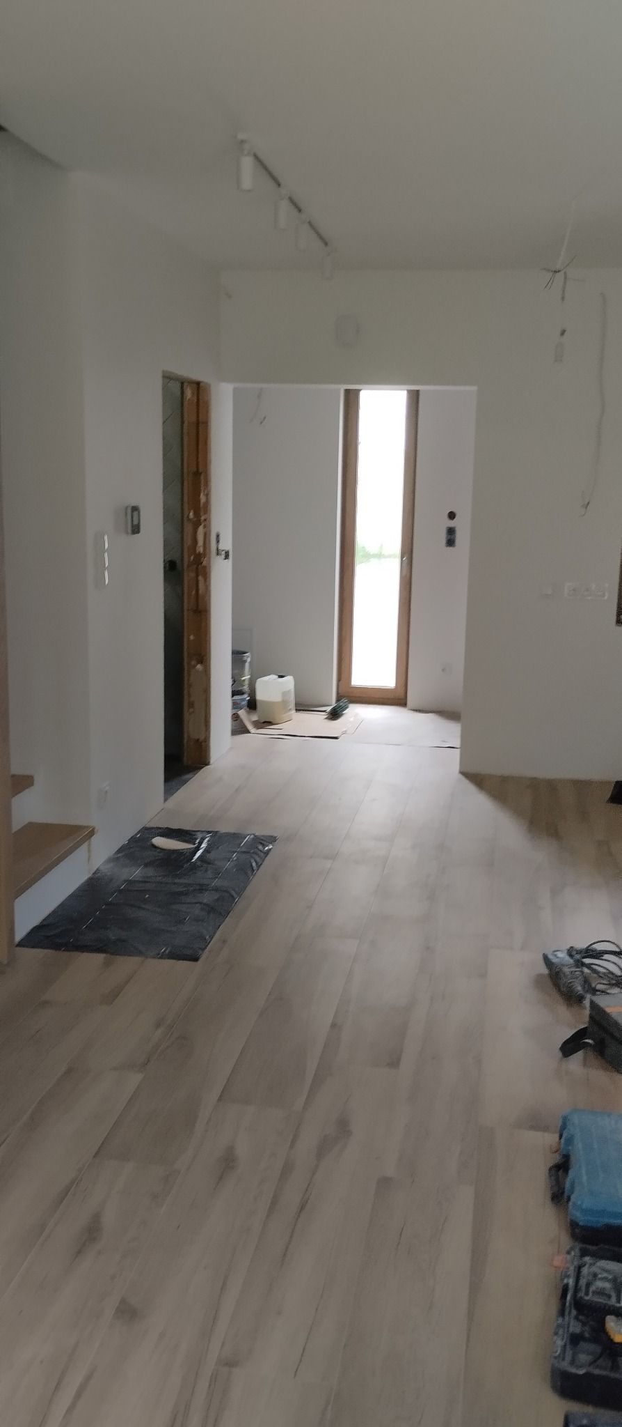 Jasne panele podłogowe ułożone w przestronnym, białym wnętrzu. Widoczne narzędzia i materiały budowlane, sugerujące trwający proces wykończenia.