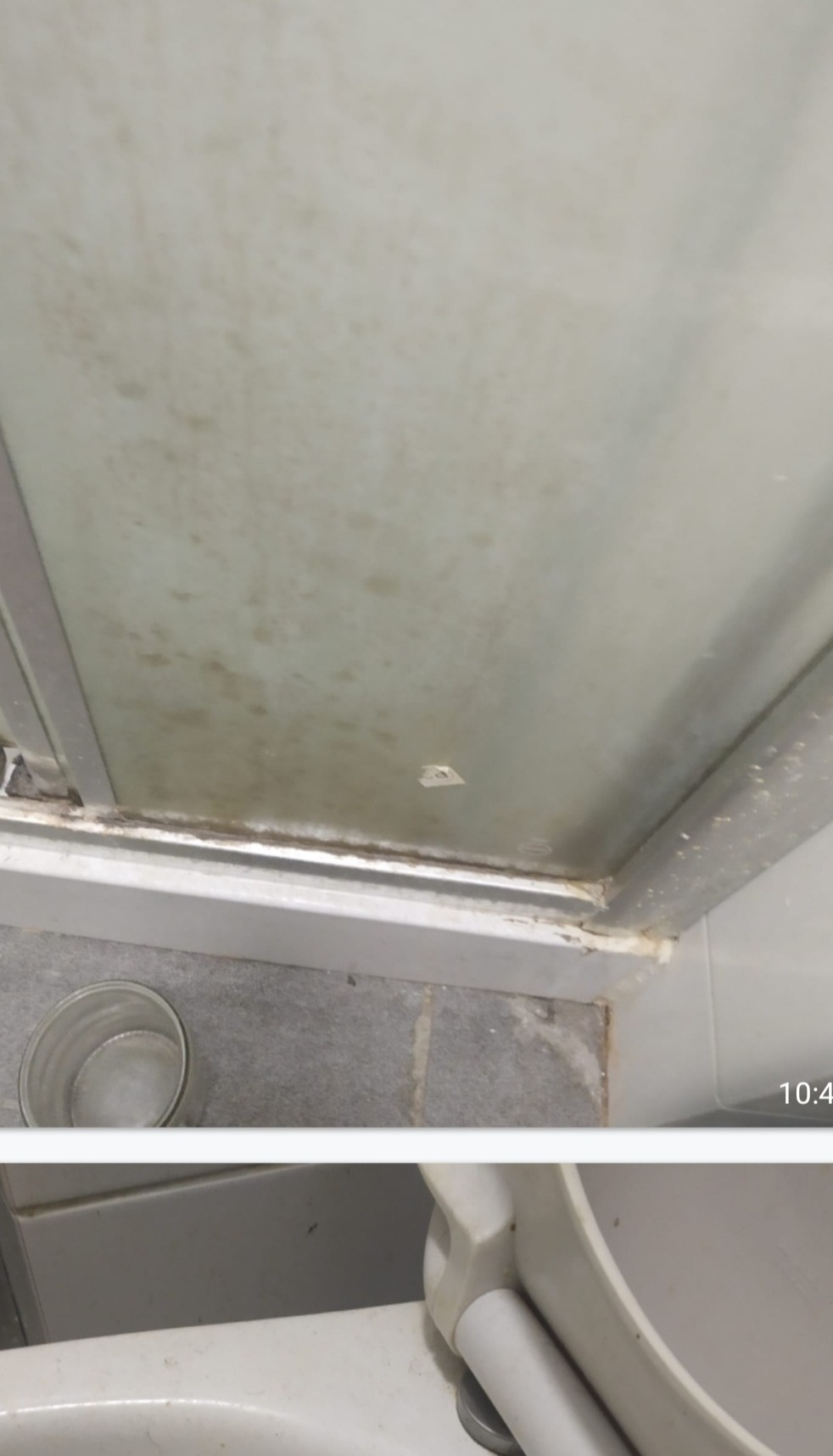 Zabrudzona, zapleśniała kabina prysznicowa z widocznym osadem, kamieniem i resztkami po mydle, zarys dolnej części toalety w dolnej części kadru.