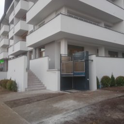 ERALIFT - Zewnętrzna platforma schodowa dla osób z niepełnosprawnościami, zamontowana przy nowoczesnym budynku mieszkalnym z balkonami, widoczna z poziomu chodnika.