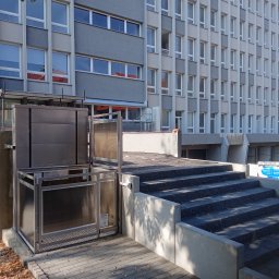 ERALIFT - Zewnętrzna platforma schodowa dla osób niepełnosprawnych, zamontowana przy schodach budynku wielorodzinnego, z widoczną metalową konstrukcją i szybą ochronną.